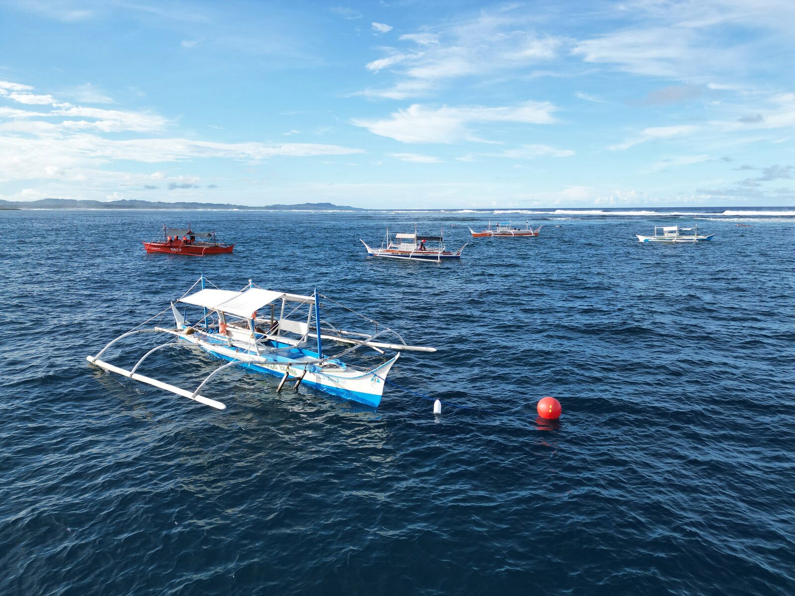 A bangka tied to a red mooring buoy instead of anchoring on the reef