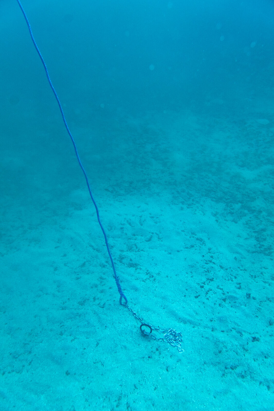 A mooring rope running down to a helix anchor in the sand